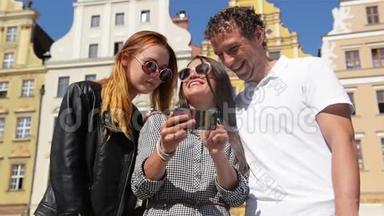 两个女孩和一个男人的户外肖像，黑发手拿黑色手机。三个朋友在用智能手机